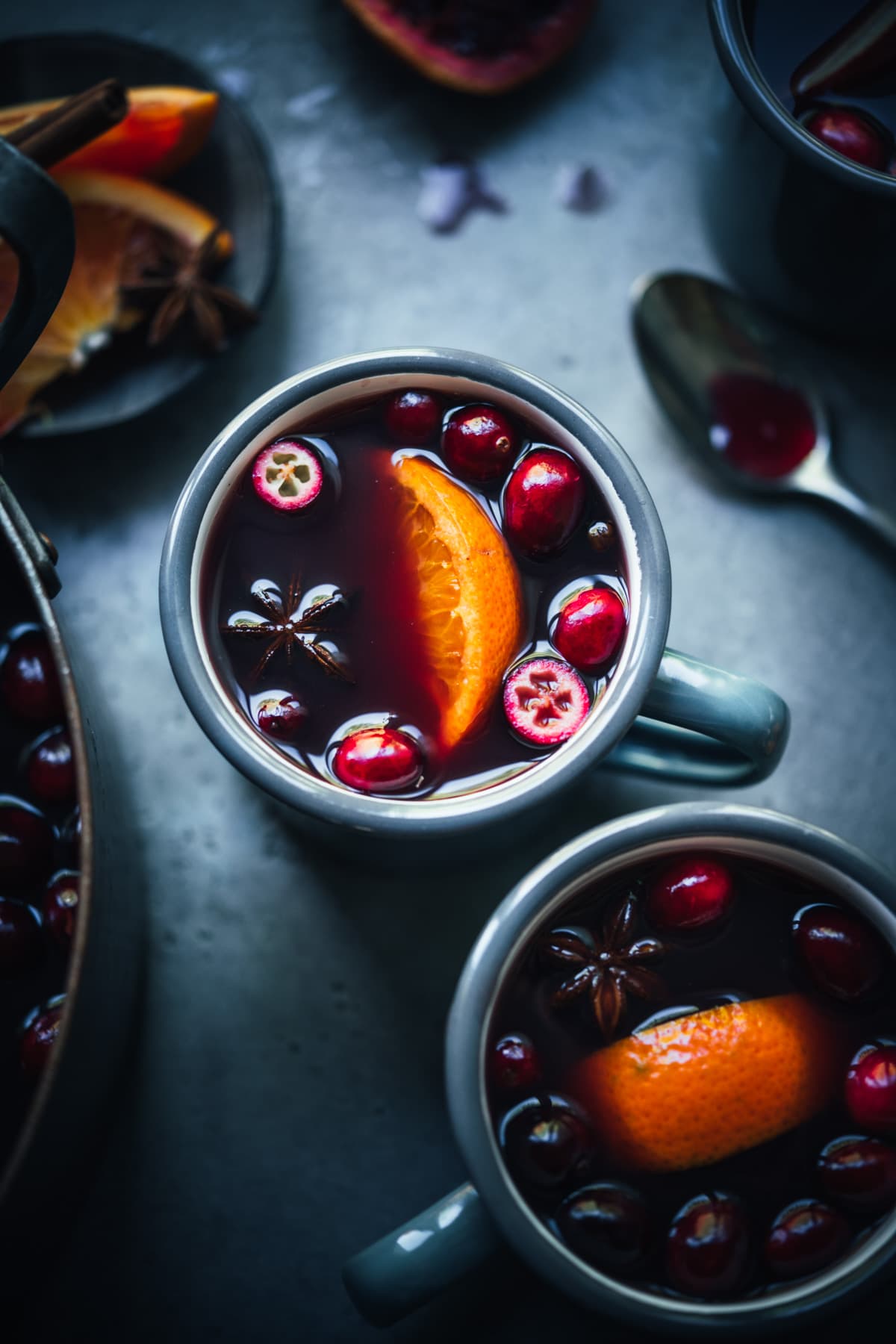 overhead view of homemade citrus mulled wine in grey mugs garnished with cranberries, star anise and orange slices.