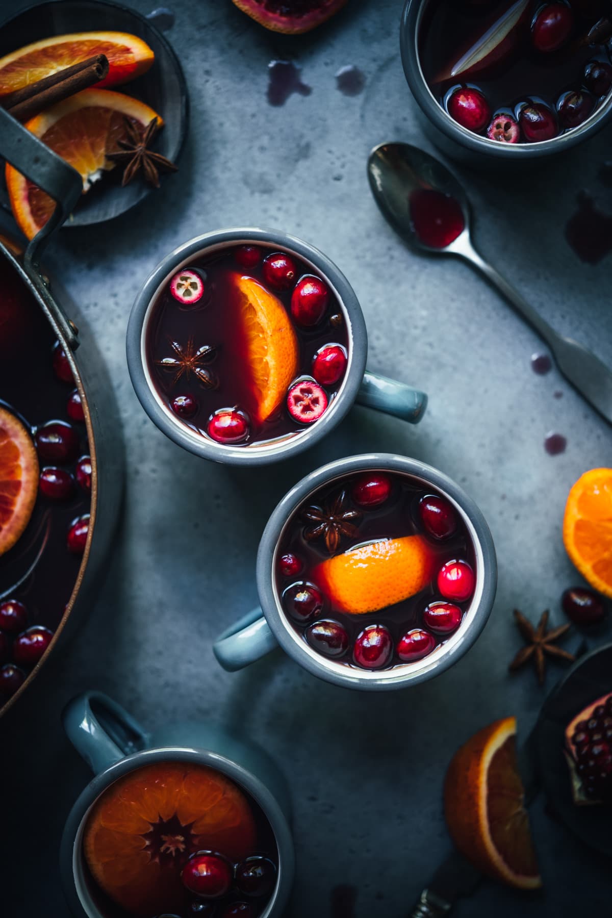 overhead view of homemade citrus mulled wine in grey mugs garnished with cranberries and orange slices. 