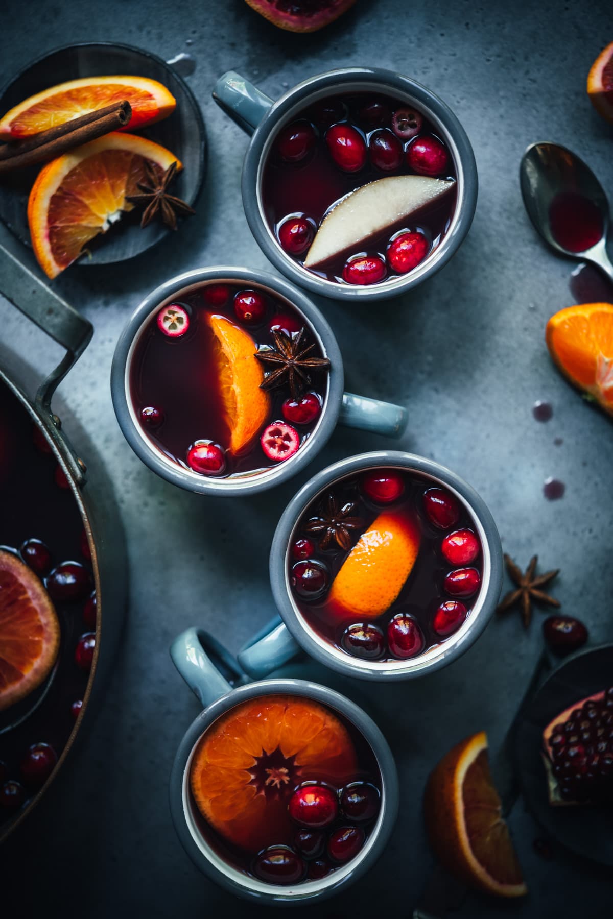 overhead view of homemade citrus mulled wine in grey mugs garnished with cranberries, star anise and orange slices.