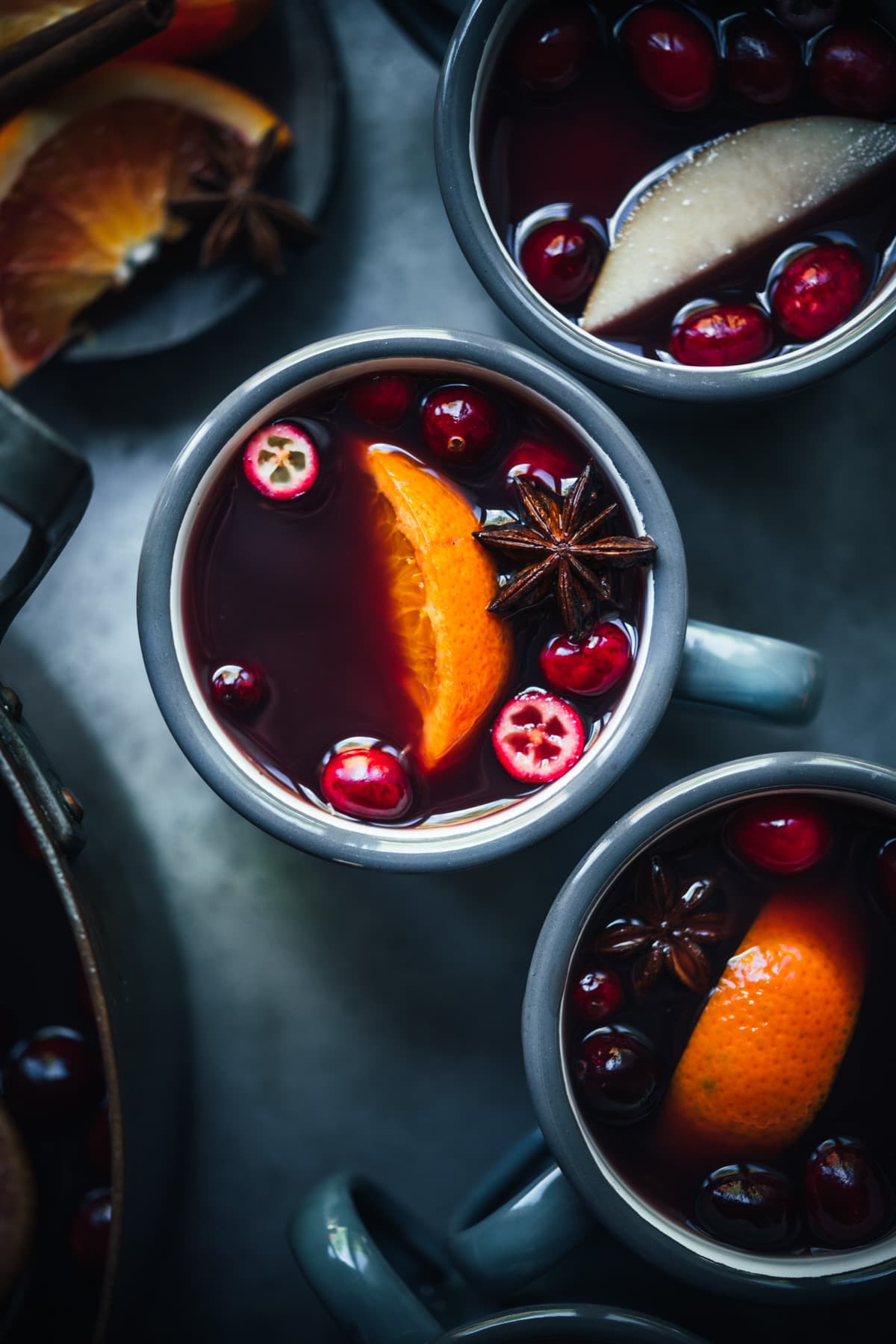 overhead view of homemade citrus mulled wine in grey mugs garnished with cranberries, star anise and orange slices.