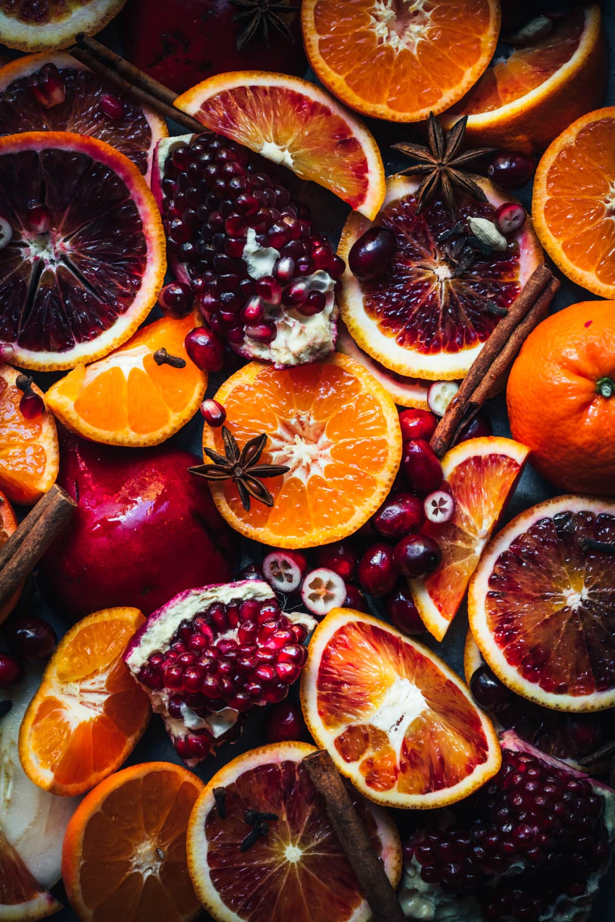 close up overhead view of ingredients for mulled wine, including citrus slices, pomegranate, cranberries and whole spices. 