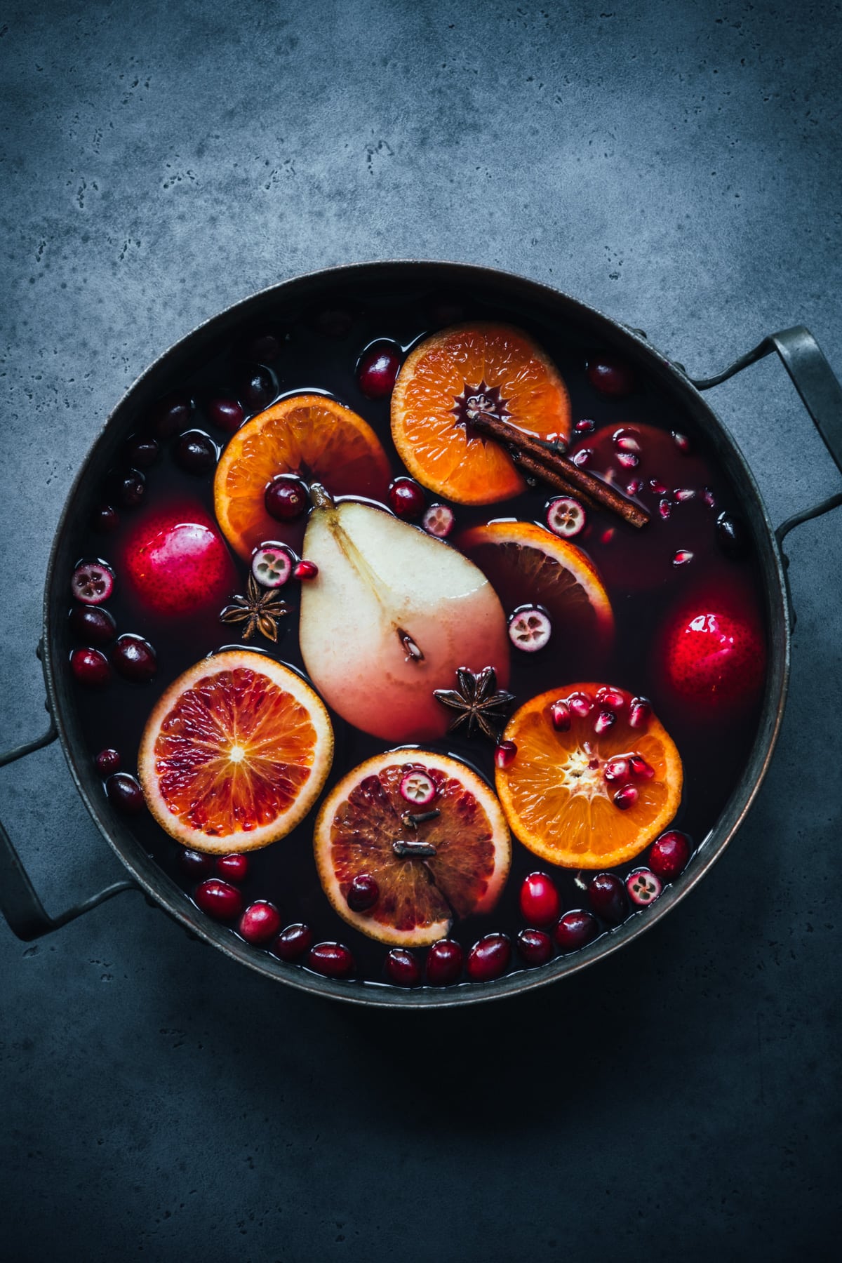 overhead view of spiced citrus and pear mulled wine in a large pot on blue backdrop. 