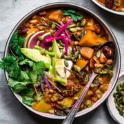 overhead view of bowl of vegan pumpkin chili topped with avocado slices, sour cream, pumpkin seeds and watermelon radish.