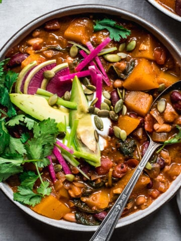 overhead view of bowl of vegan pumpkin chili topped with avocado slices, sour cream, pumpkin seeds and watermelon radish.
