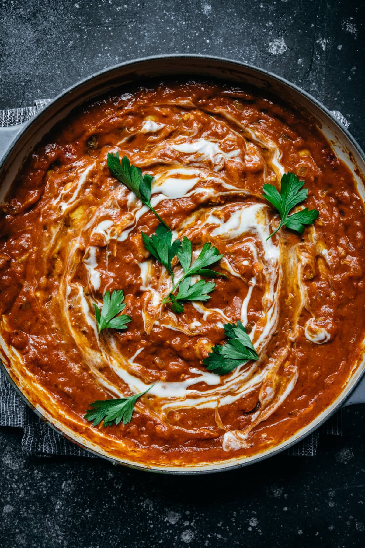 overhead view of vegan tofu tikka masala in a large pan with yogurt swirl and fresh herbs. 