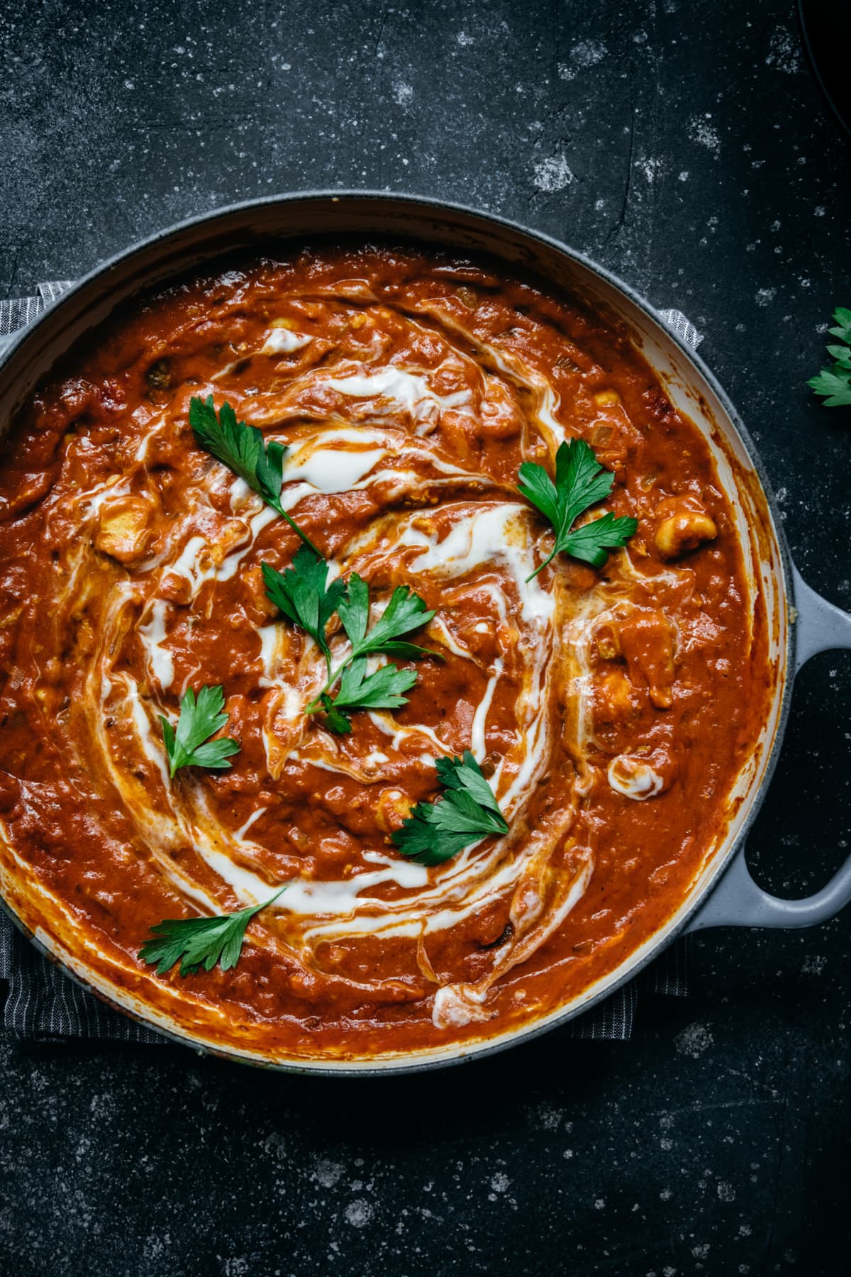 overhead view of vegan tofu tikka masala in a large pan with yogurt swirl and fresh herbs. 