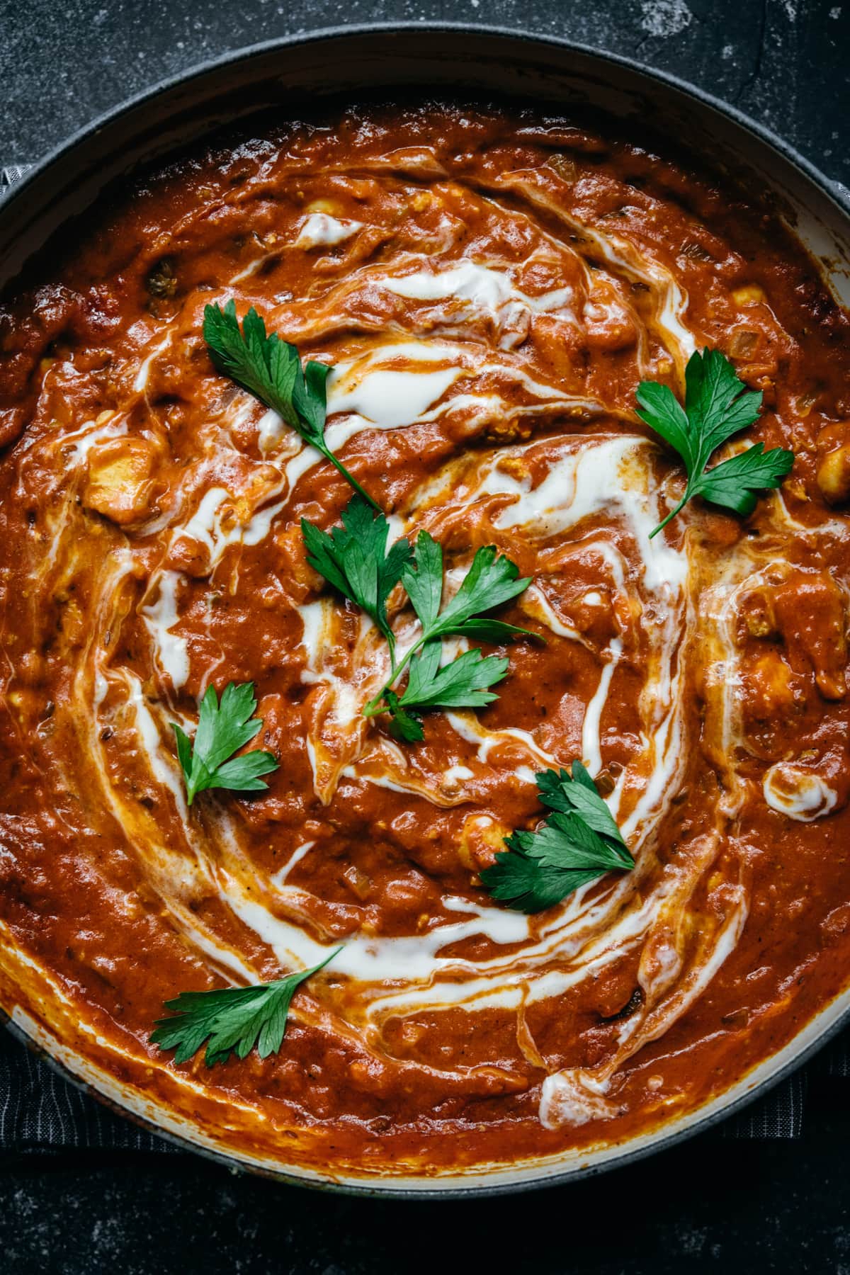 overhead view of vegan tofu tikka masala in a large pan with yogurt swirl and fresh herbs. 