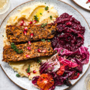 overhead view of vegan meatloaf on a white plate over mashed potatoes with cranberry sauce and salad on the side.