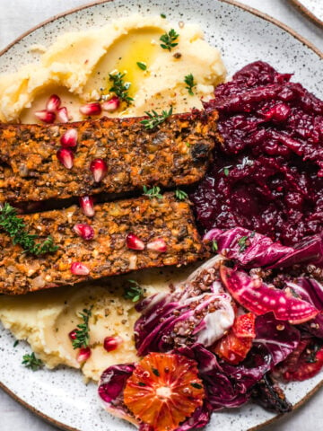 overhead view of vegan meatloaf on a white plate over mashed potatoes with cranberry sauce and salad on the side.