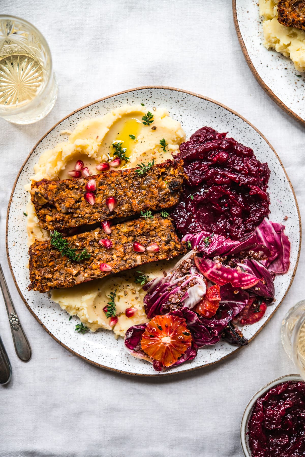 overhead view of vegan meatloaf on a white plate over mashed potatoes with cranberry sauce and salad on the side. 