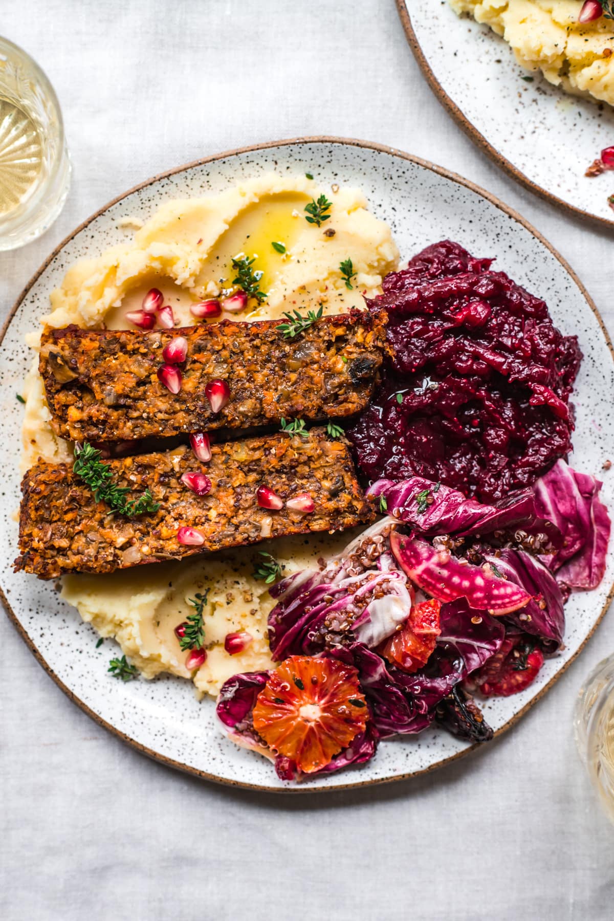 overhead view of vegan meatloaf on a white plate over mashed potatoes with cranberry sauce and salad on the side. 