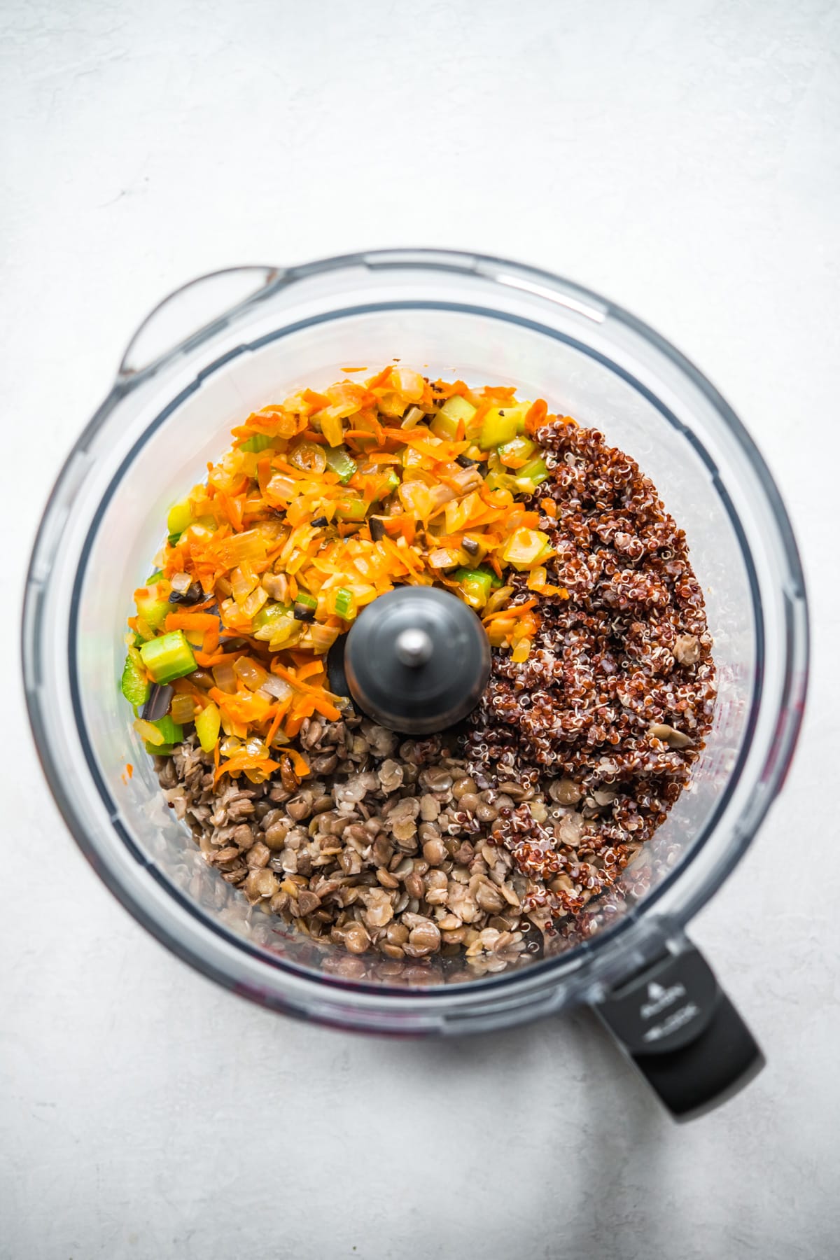 overhead view of cooked vegetables, lentils and quinoa in a food processor. 