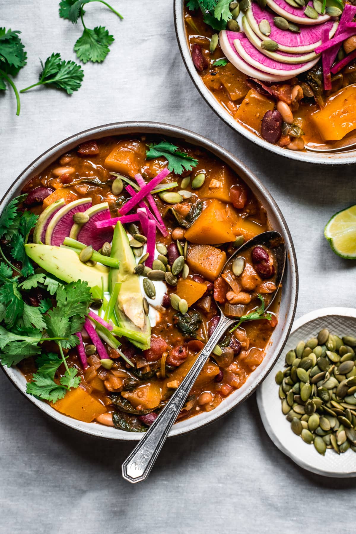 overhead view of bowl of vegan pumpkin chili topped with avocado slices, sour cream, pumpkin seeds and watermelon radish.