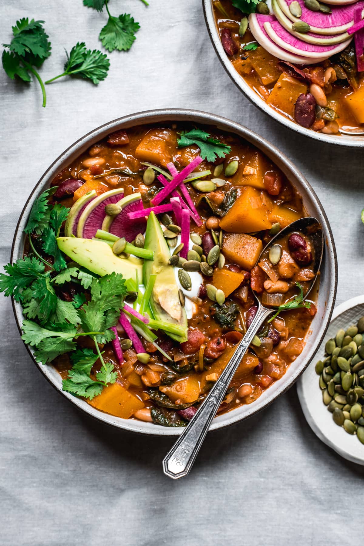 overhead view of bowl of vegan pumpkin chili topped with avocado slices, sour cream, pumpkin seeds and watermelon radish.