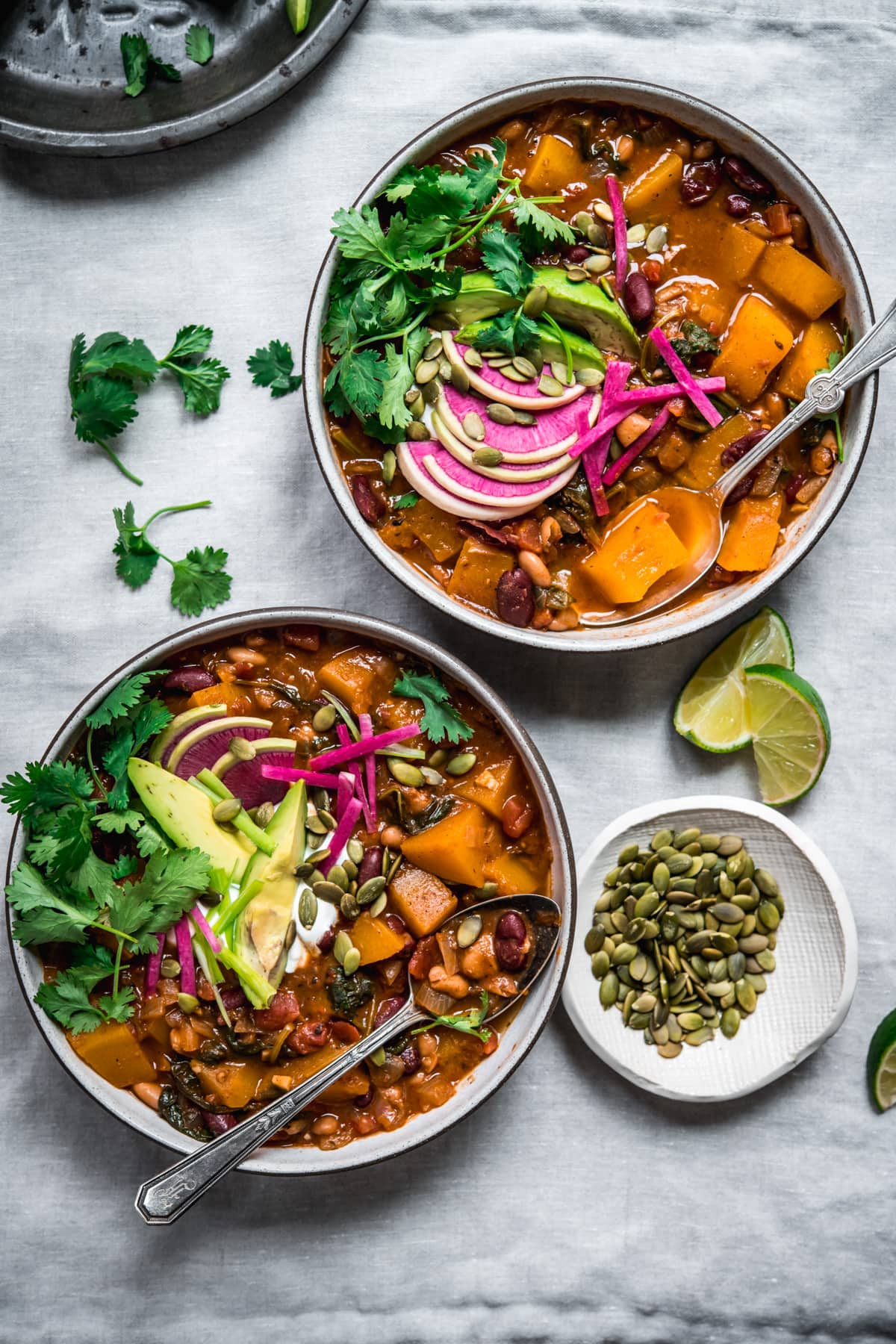 overhead view of bowls of vegan pumpkin chili topped with avocado slices, sour cream, pumpkin seeds and watermelon radish.