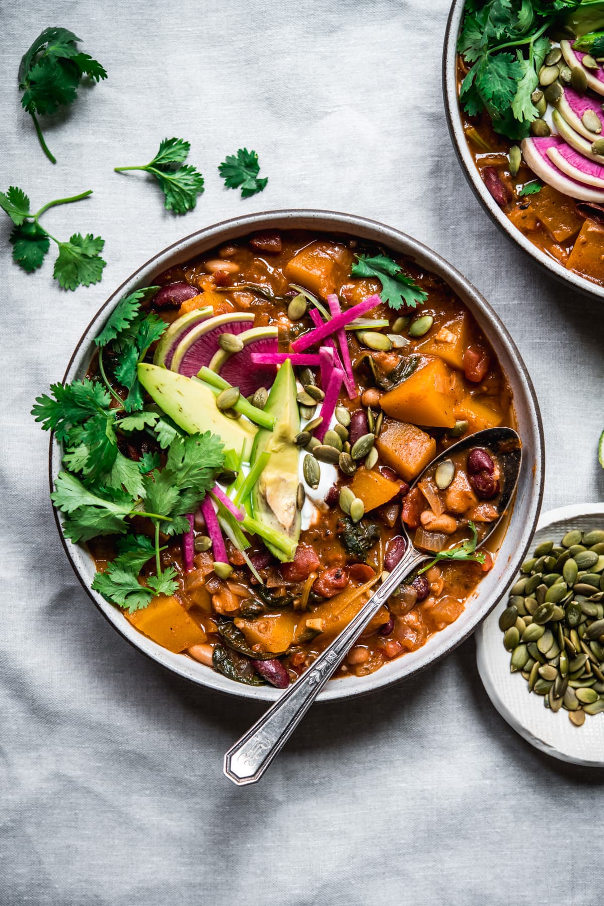 overhead view of bowl of vegan pumpkin chili topped with avocado slices, sour cream, pumpkin seeds and watermelon radish.