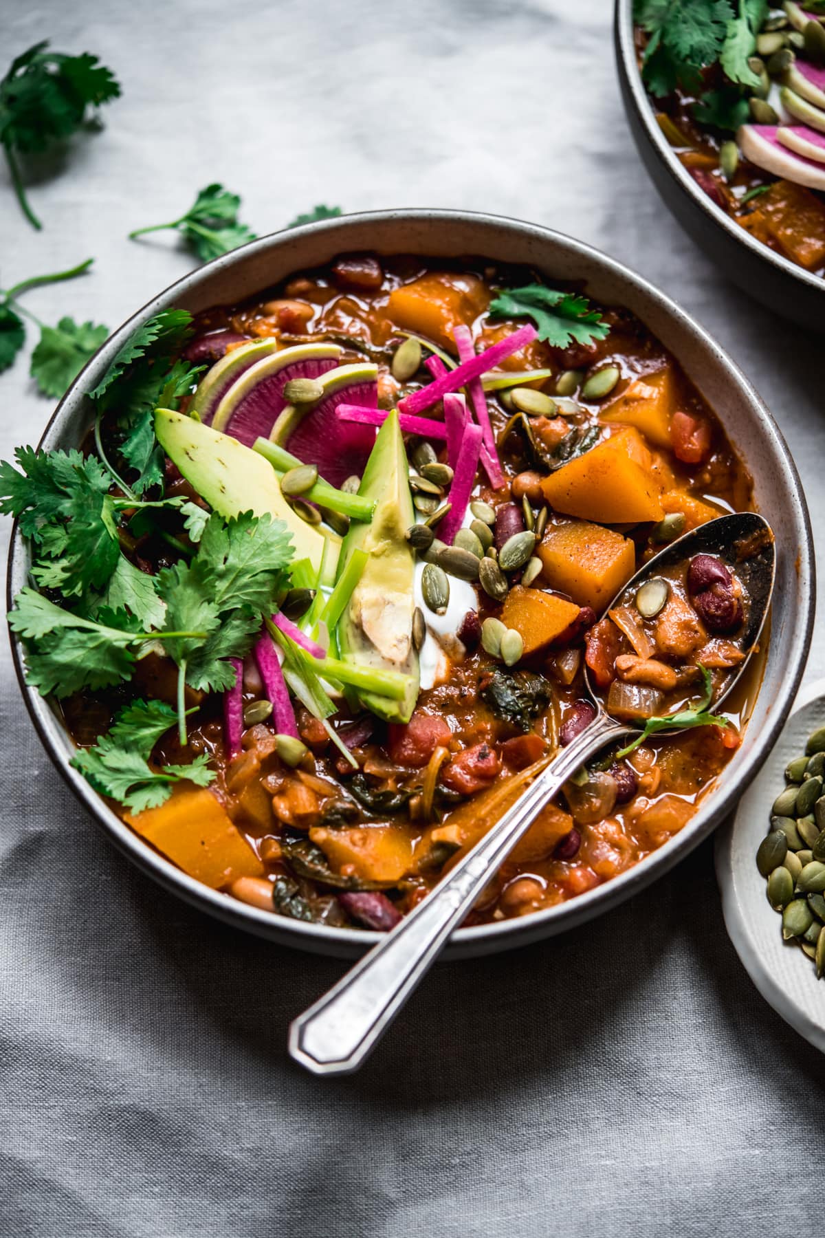 overhead view of bowl of vegan pumpkin chili topped with avocado slices, sour cream, pumpkin seeds and watermelon radish.