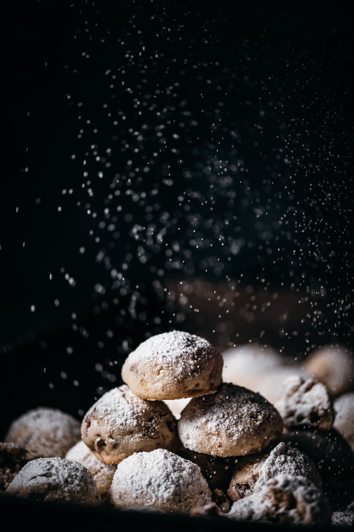 stack of pecan snowball cookies being dusted with powdered sugar. 