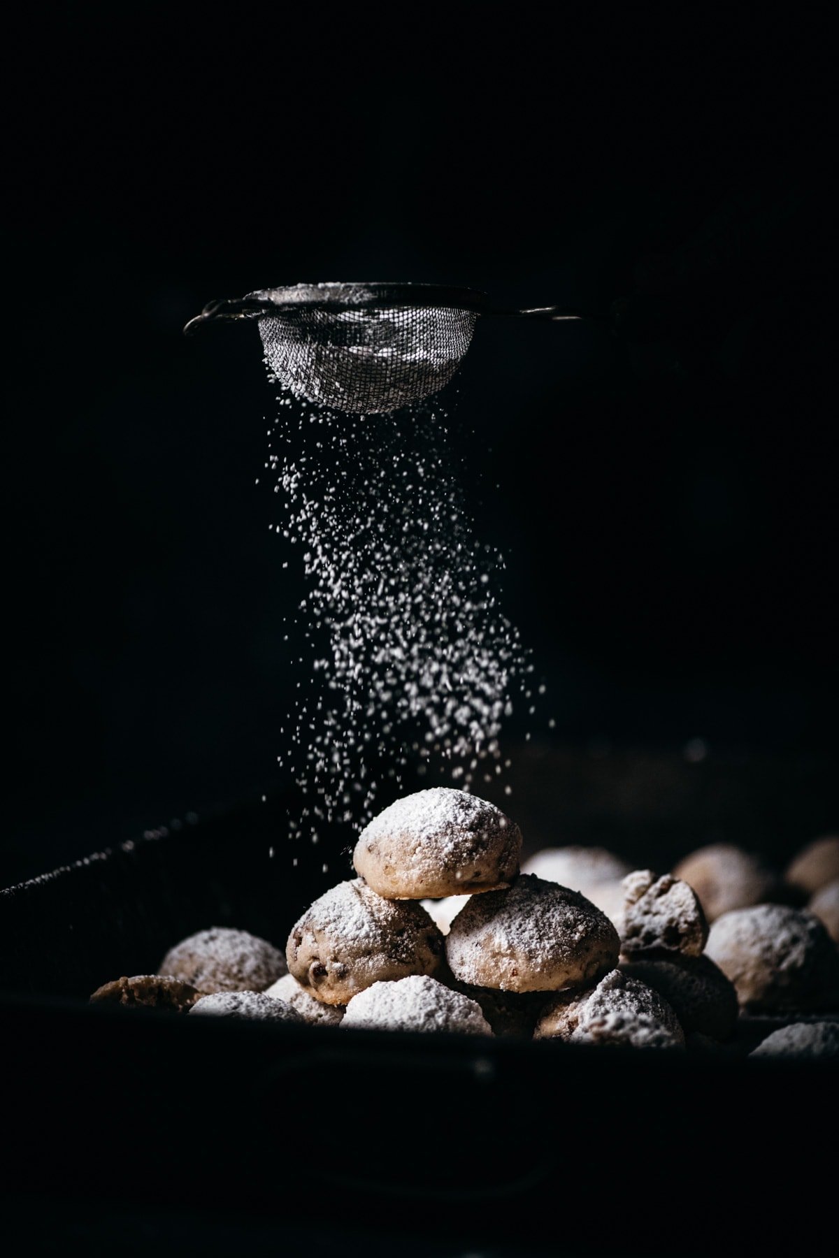 stack of pecan snowball cookies being dusted with powdered sugar. 