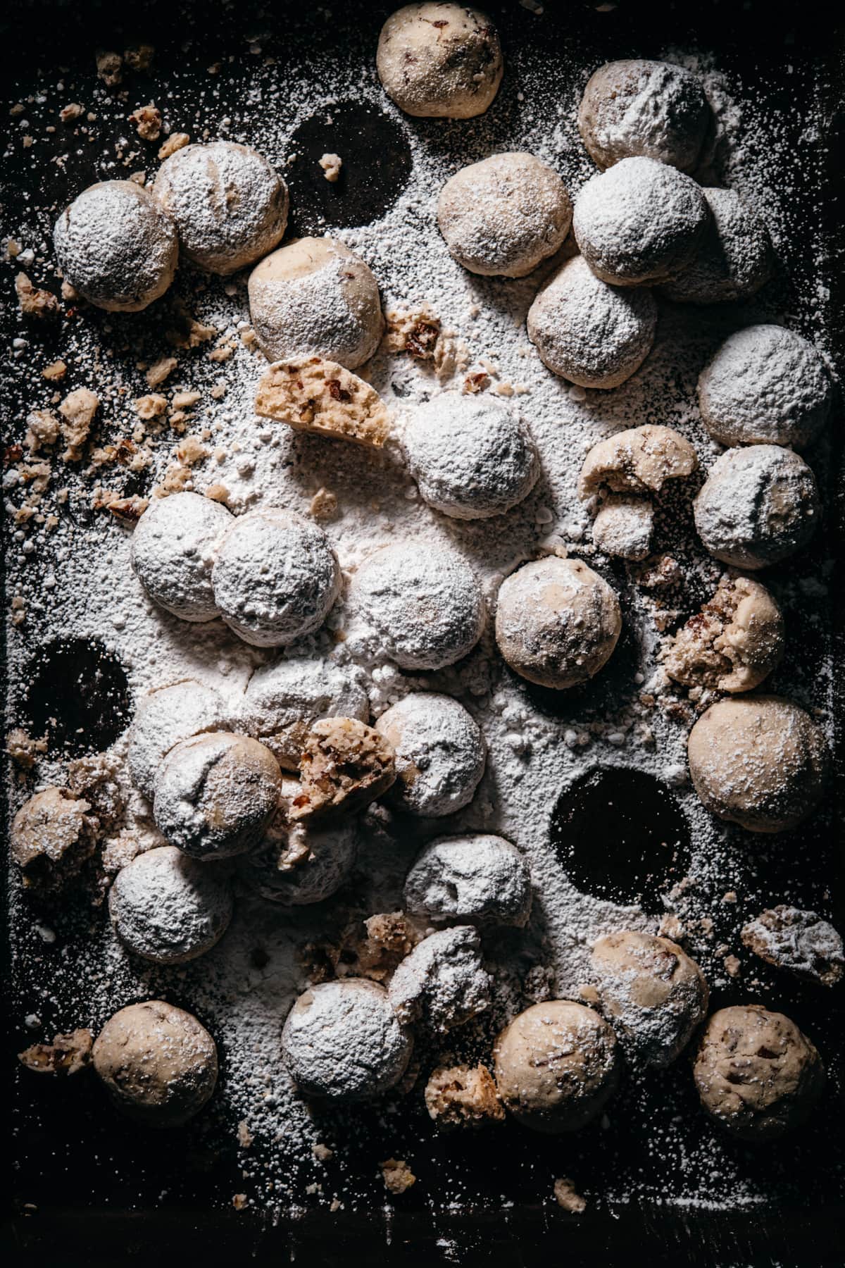 overhead view of vegan pecan snowball cookies on dark cookie sheet.