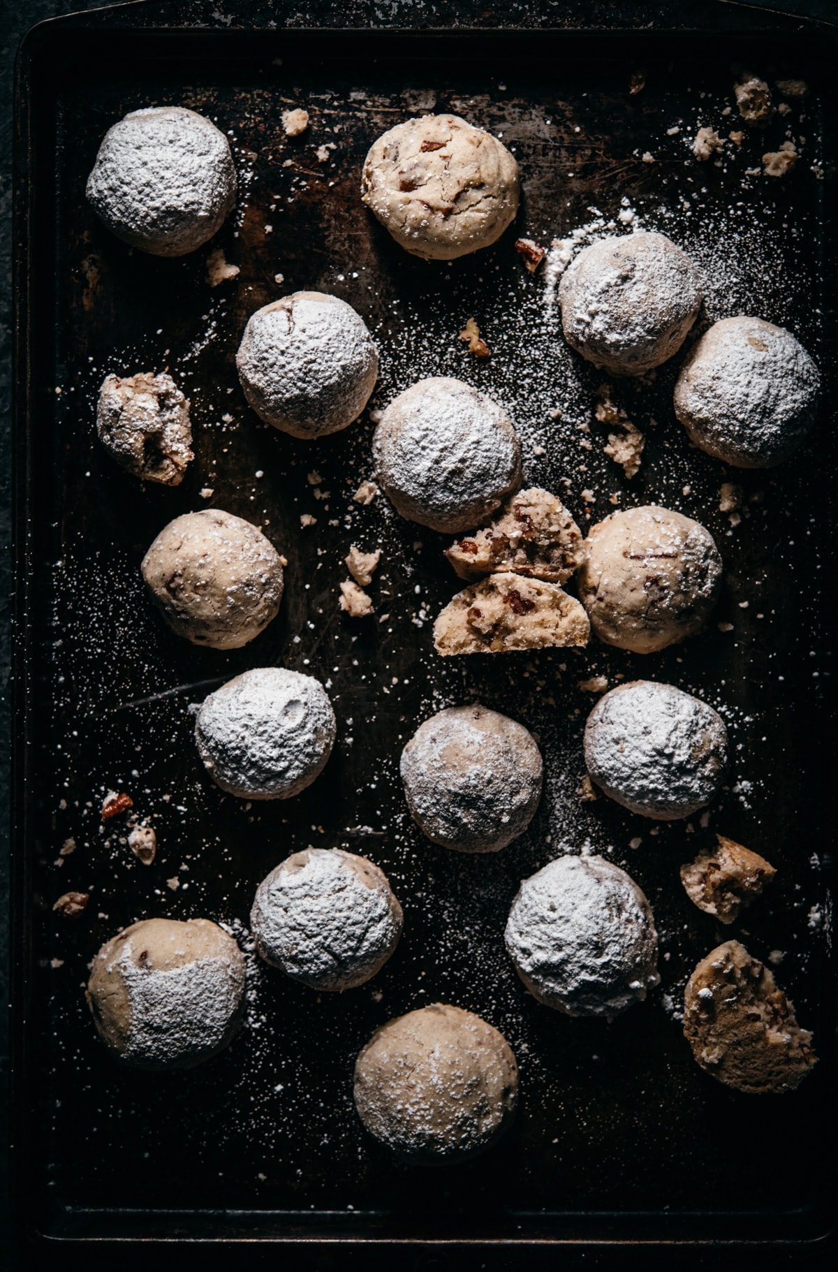 overhead view of vegan pecan snowball cookies on dark cookie sheet.