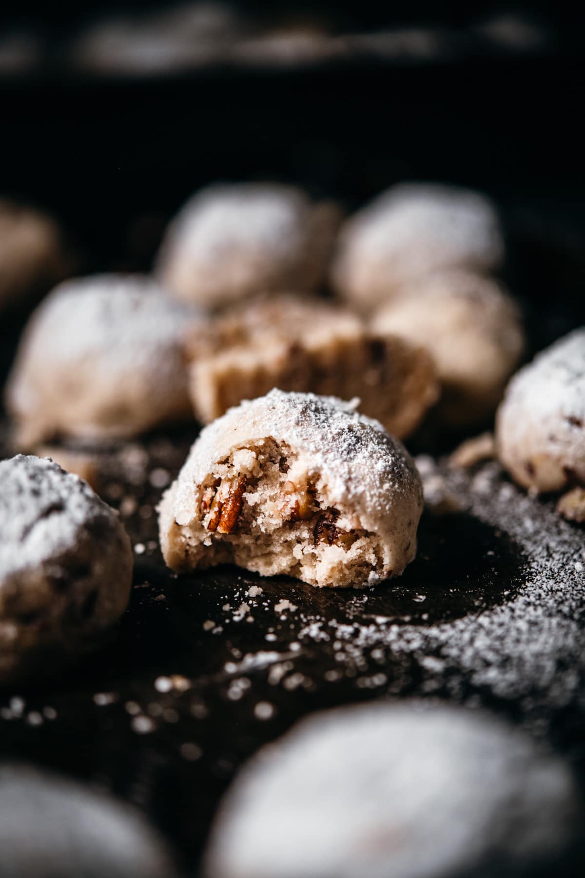 close up view of vegan pecan snowball cookie with bite taken out. 