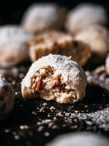 close up view of vegan pecan snowball cookie with bite taken out.