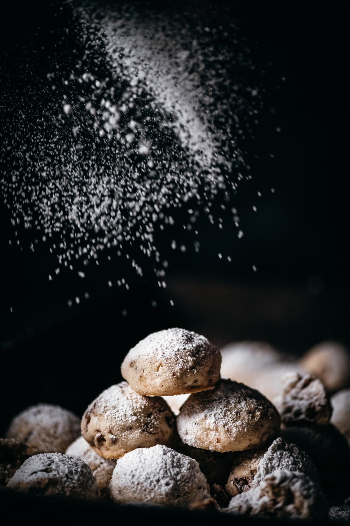 stack of pecan snowball cookies being dusted with powdered sugar. 