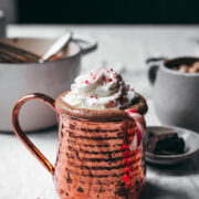 side view of vegan peppermint hot chocolate in copper mug topped with whipped cream and candy canes.