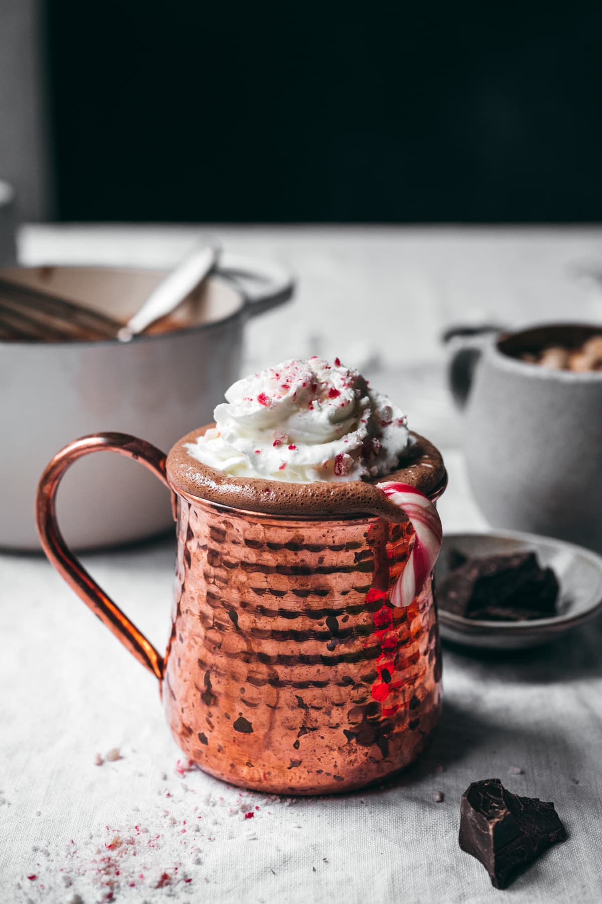 side view of vegan peppermint hot chocolate in copper mug topped with whipped cream and candy canes. 