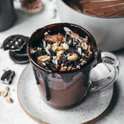 side view of peanut butter hot chocolate with chocolate and peanut toppings and fudge coming down side of mug.