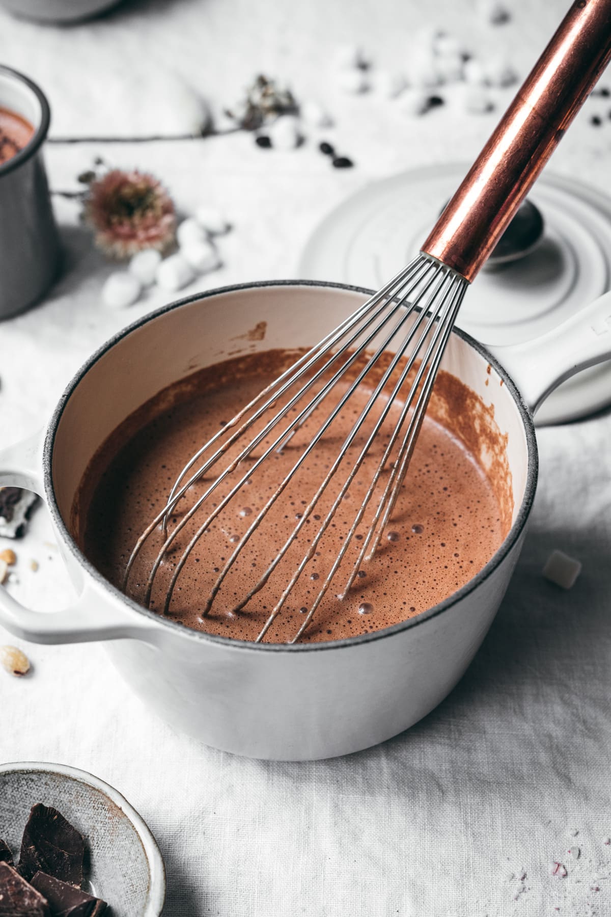 side view of mocha hot chocolate in a white saucepan with whisk.