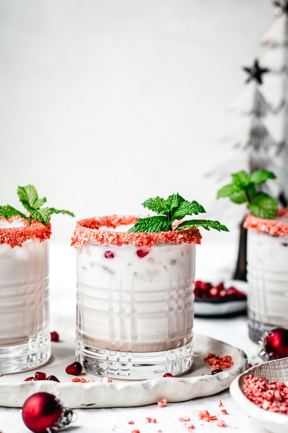 close up side view of vegan peppermint white russian cocktail with candy cane rim and fresh mint garnish. 
