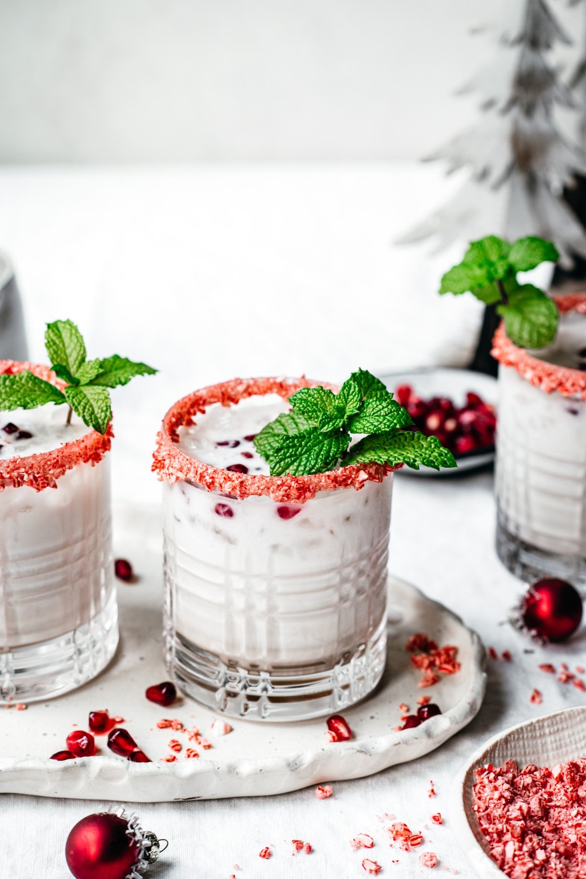 close up side view of vegan peppermint white russian cocktail with candy cane rim and fresh mint garnish. 