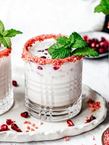 close up side view of vegan peppermint white russian cocktail with candy cane rim and fresh mint garnish.