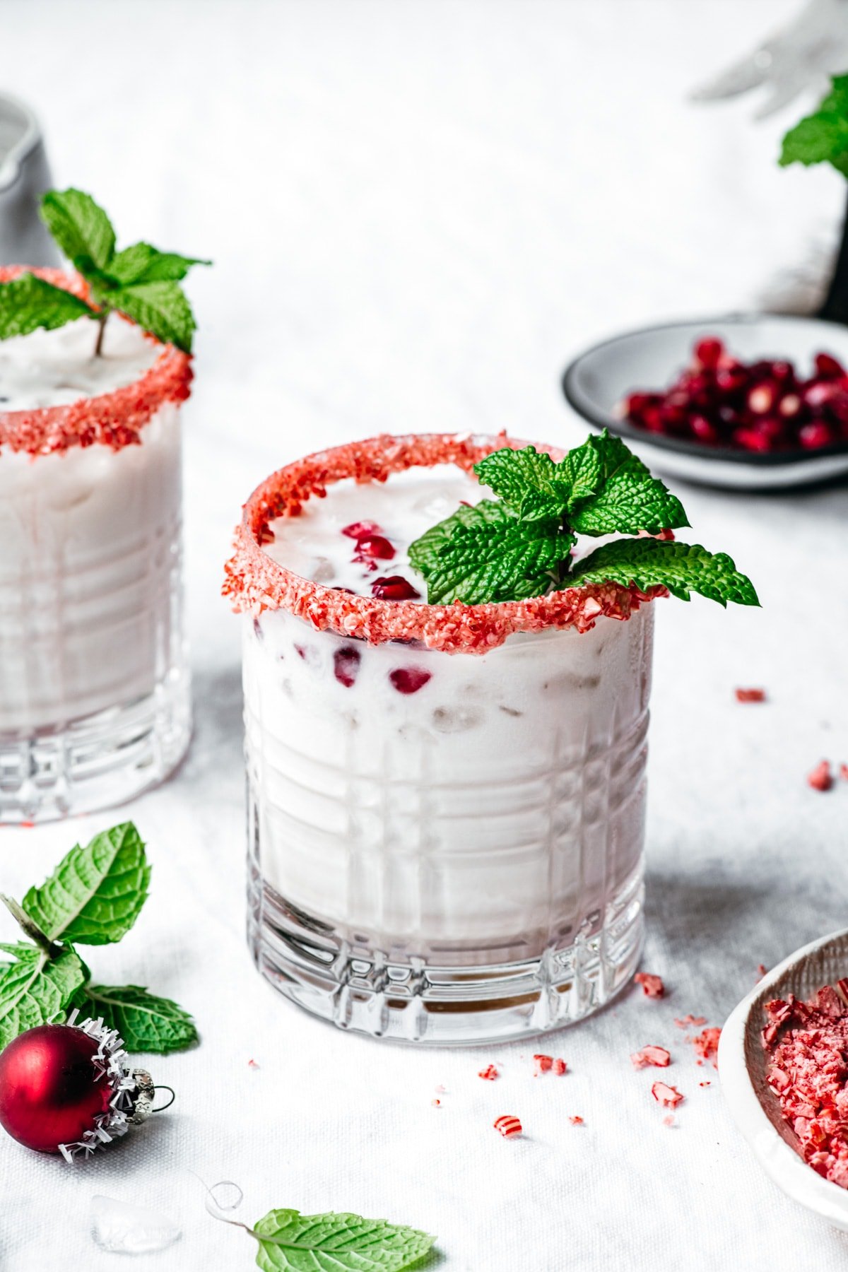 close up side view of vegan peppermint white russian cocktail with candy cane rim and fresh mint garnish. 