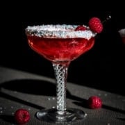 close up side view of shimmery raspberry rosé cocktail with sprinkle rim in antique cocktail glass.