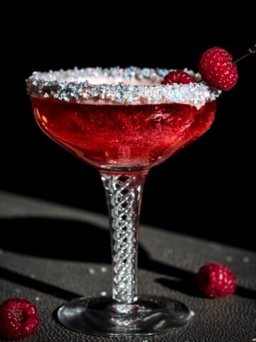 close up side view of shimmery raspberry rosé cocktail with sprinkle rim in antique cocktail glass.