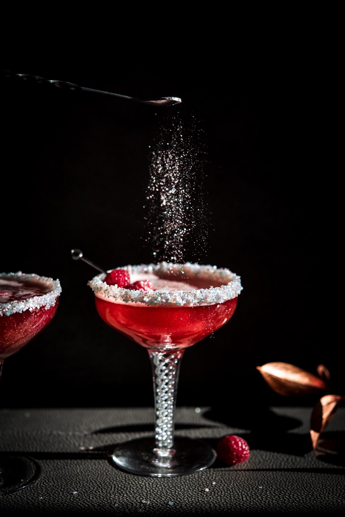 shimmer dust falling on a raspberry rosé santa baby holiday cocktail in antique coupe glass.