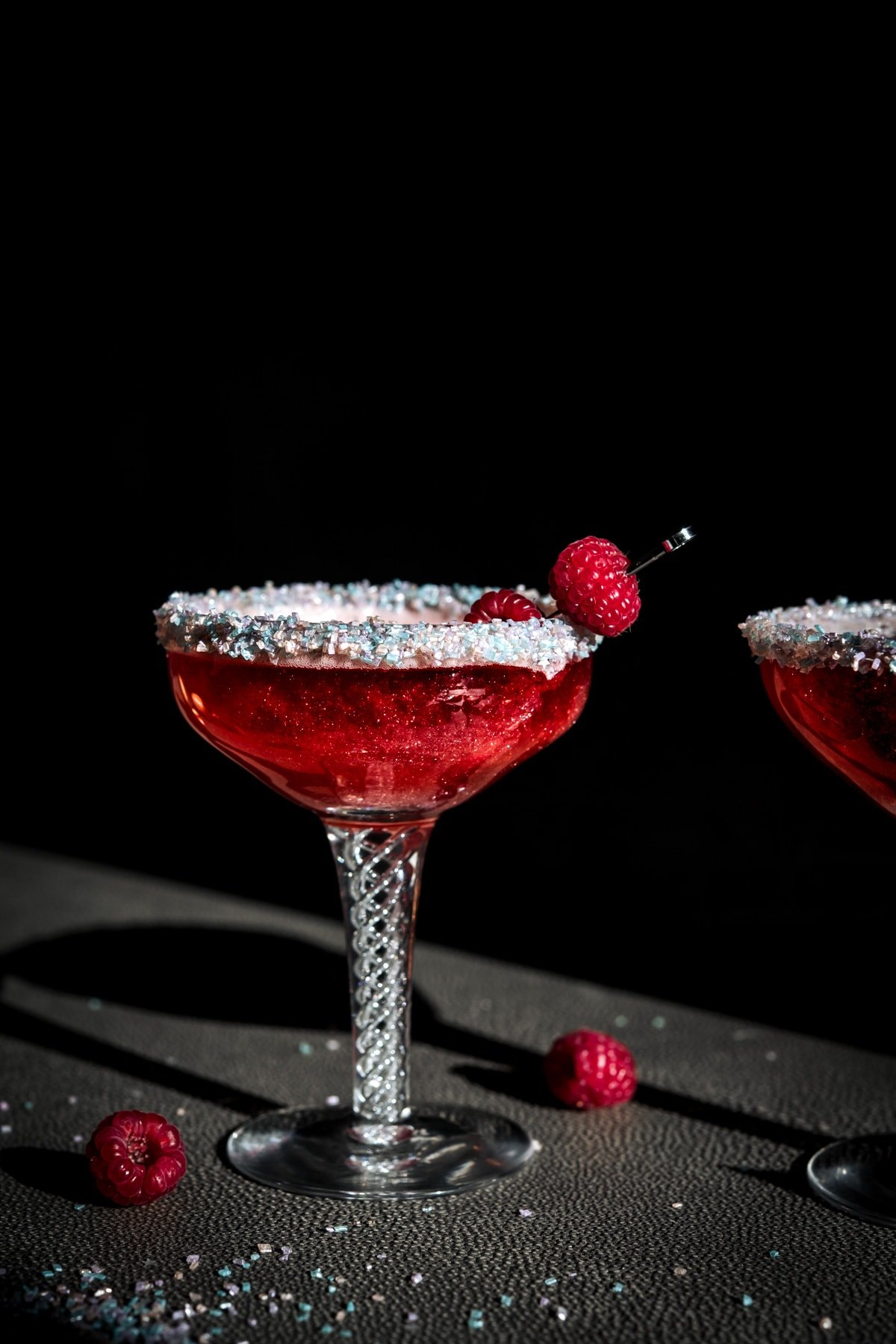 close up side view of shimmery raspberry rosé cocktail with sprinkle rim in antique cocktail glass. 