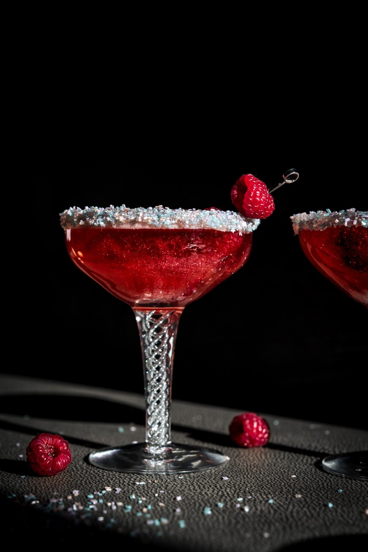 close up side view of shimmery raspberry rosé cocktail with sprinkle rim in antique cocktail glass. 