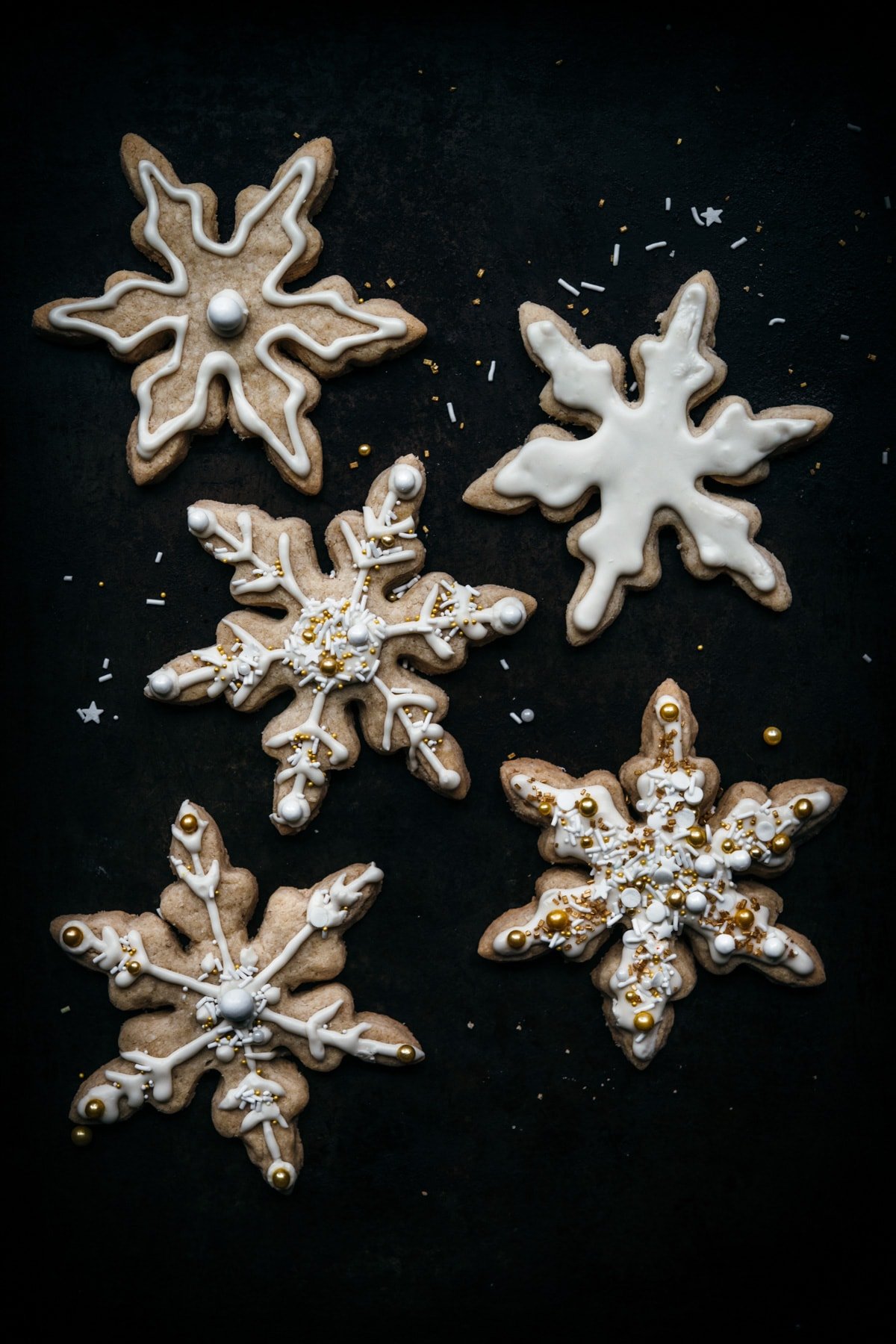 overhead view of vegan snowflake sugar cookies on dark backdrop.