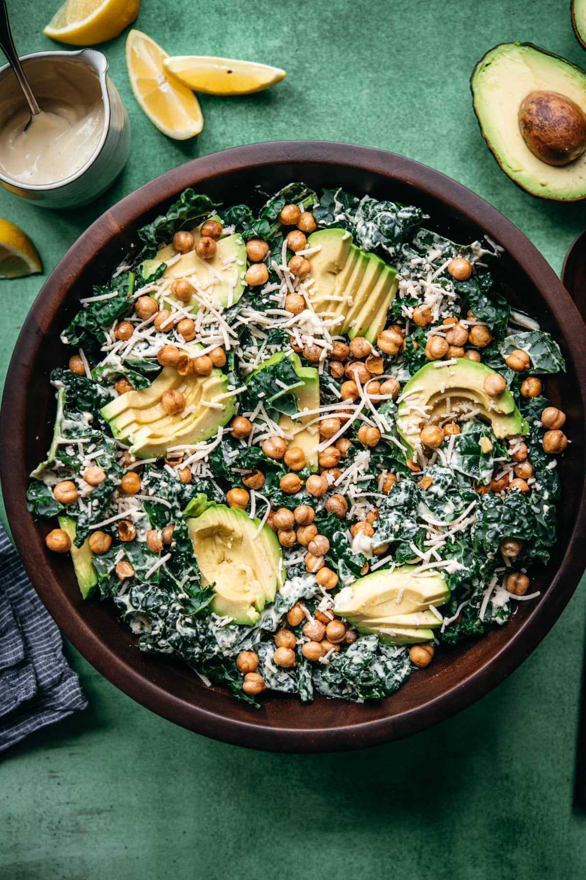 overhead view of vegan kale caesar salad in a large wood bowl topped with avocado and crispy chickpeas. 