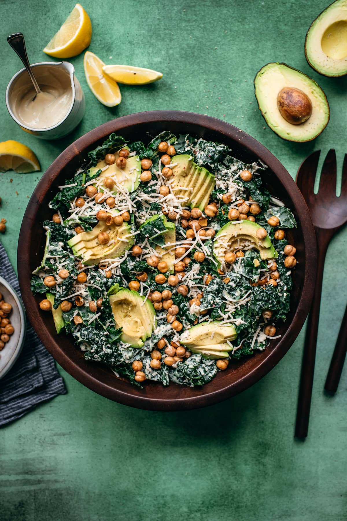 overhead view of vegan kale caesar salad in a large wood bowl topped with avocado and crispy chickpeas. 