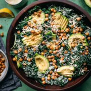 overhead view of vegan kale caesar salad in a large wood bowl topped with avocado and crispy chickpeas.