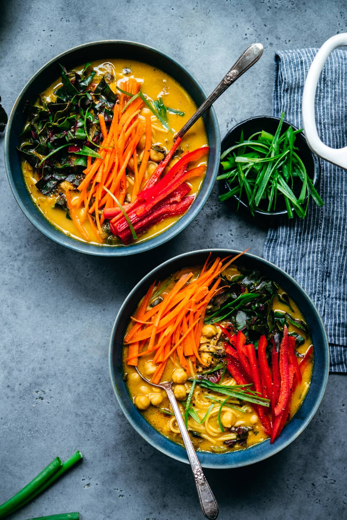overhead view of two large bowls of chickpea noodle soup topped with fresh carrots and bell pepper. 