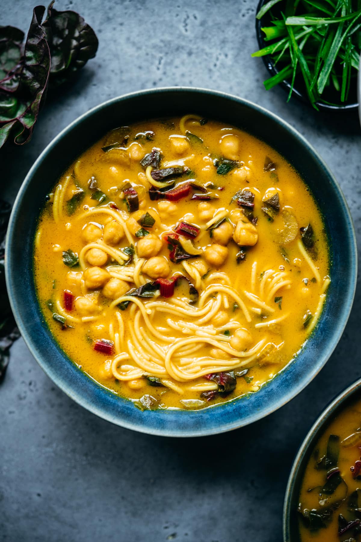 Close up overhead view of chickpea noodle soup in a blue bowl. 