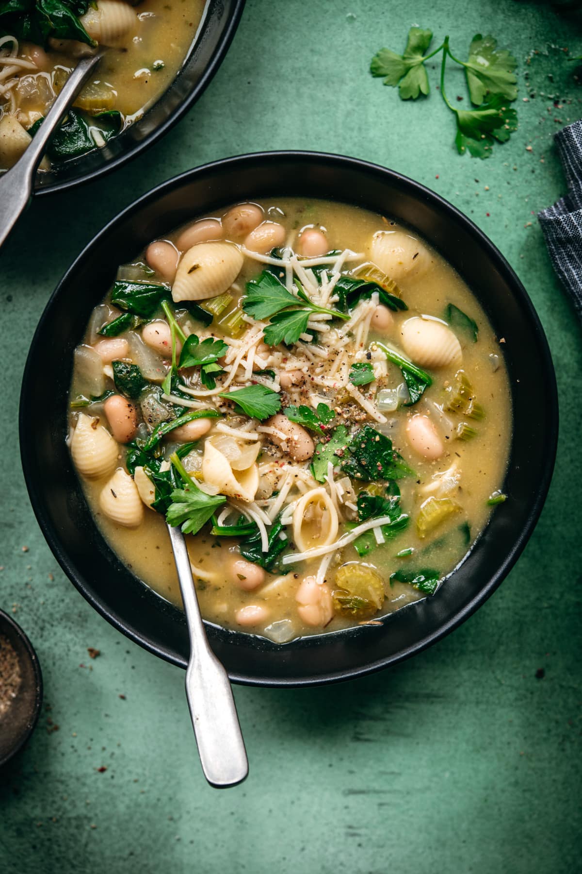 overhead view of white bean spinach soup topped with vegan parmesan in black soup bowl. 