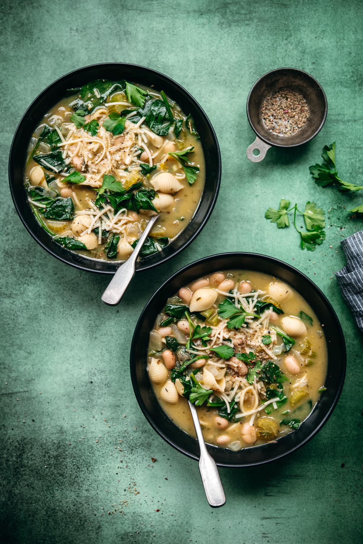 overhead view of 2 bowls of white bean spinach soup topped with vegan parmesan and parsley. 