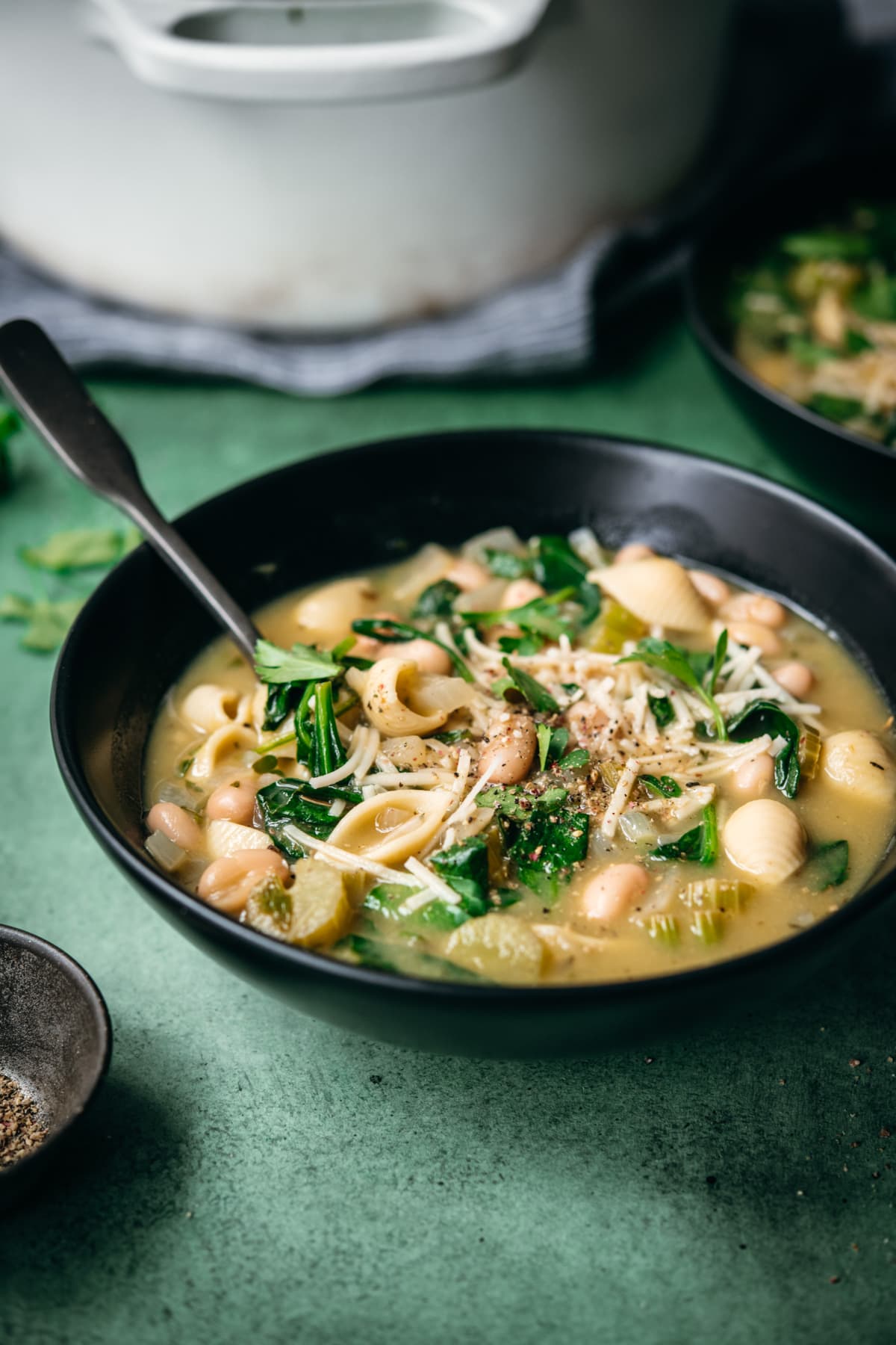 close up view of white bean spinach pasta soup in a black bowl.